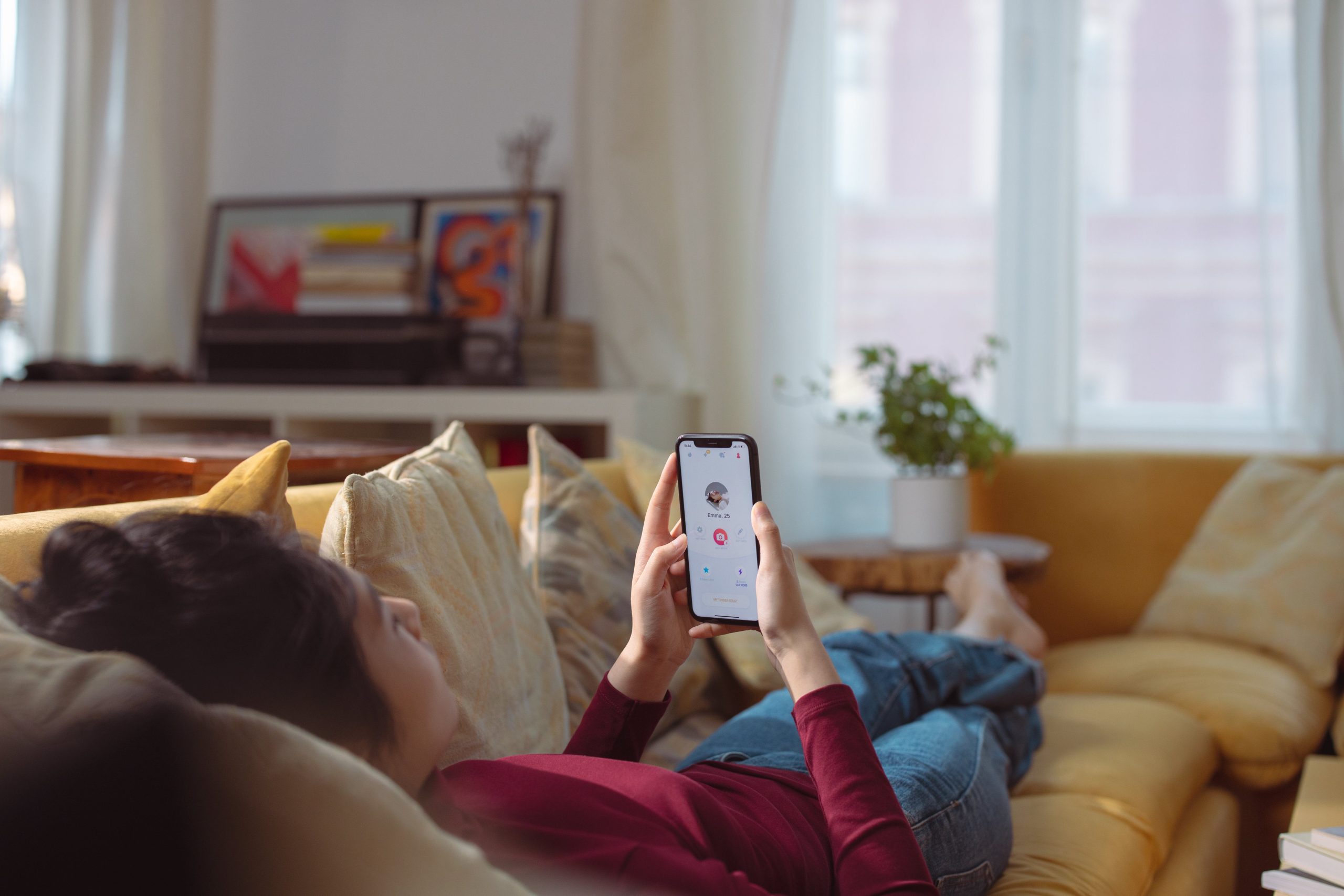 A happy woman lying on the sofa which is taking a conversation with someone on her mobile phone.