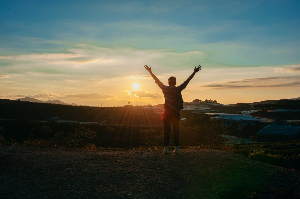 A man, with arms wide open, basking in the rising morning light, enjoying his freedom.