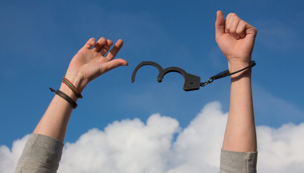 A pair of hands that have already broken free from half of the handcuffs' restraints.
