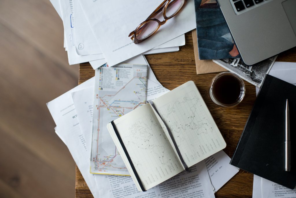 The desktop is cluttered with a computer, laptop, coffee, and various items.