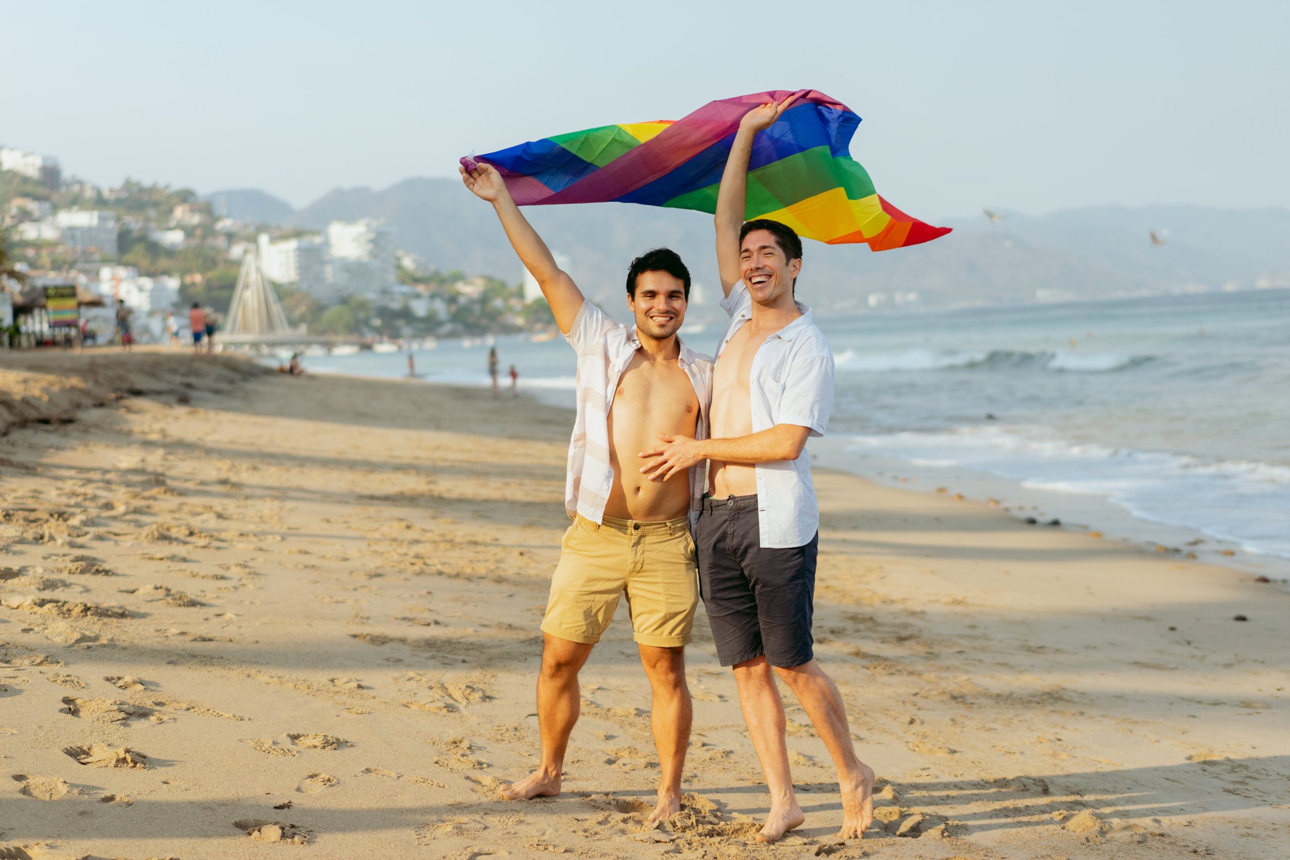 A pair of male lovers happily holding a rainbow flag on the beach