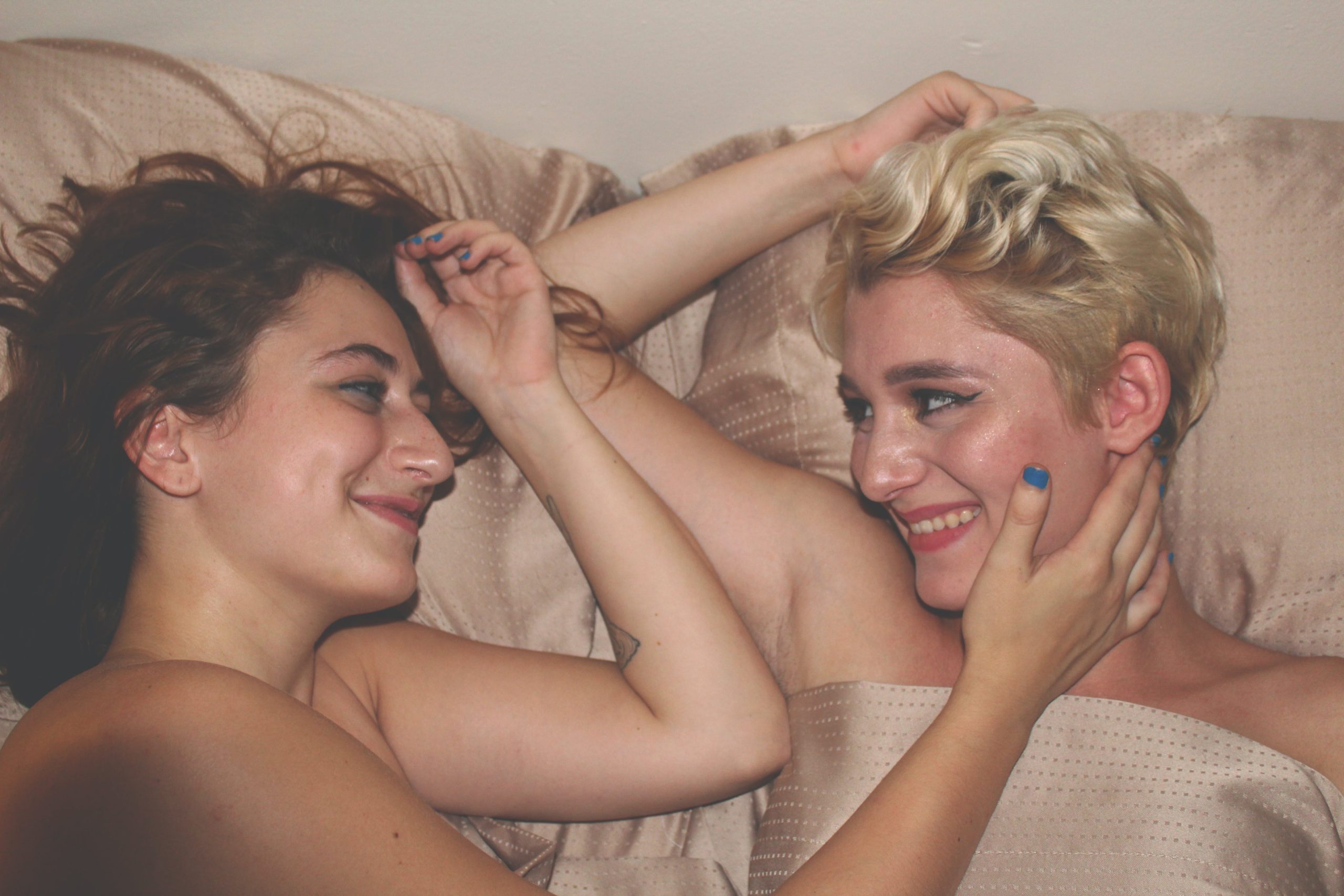 2 LGBTQ people lying on the bed looking at each other and laughing