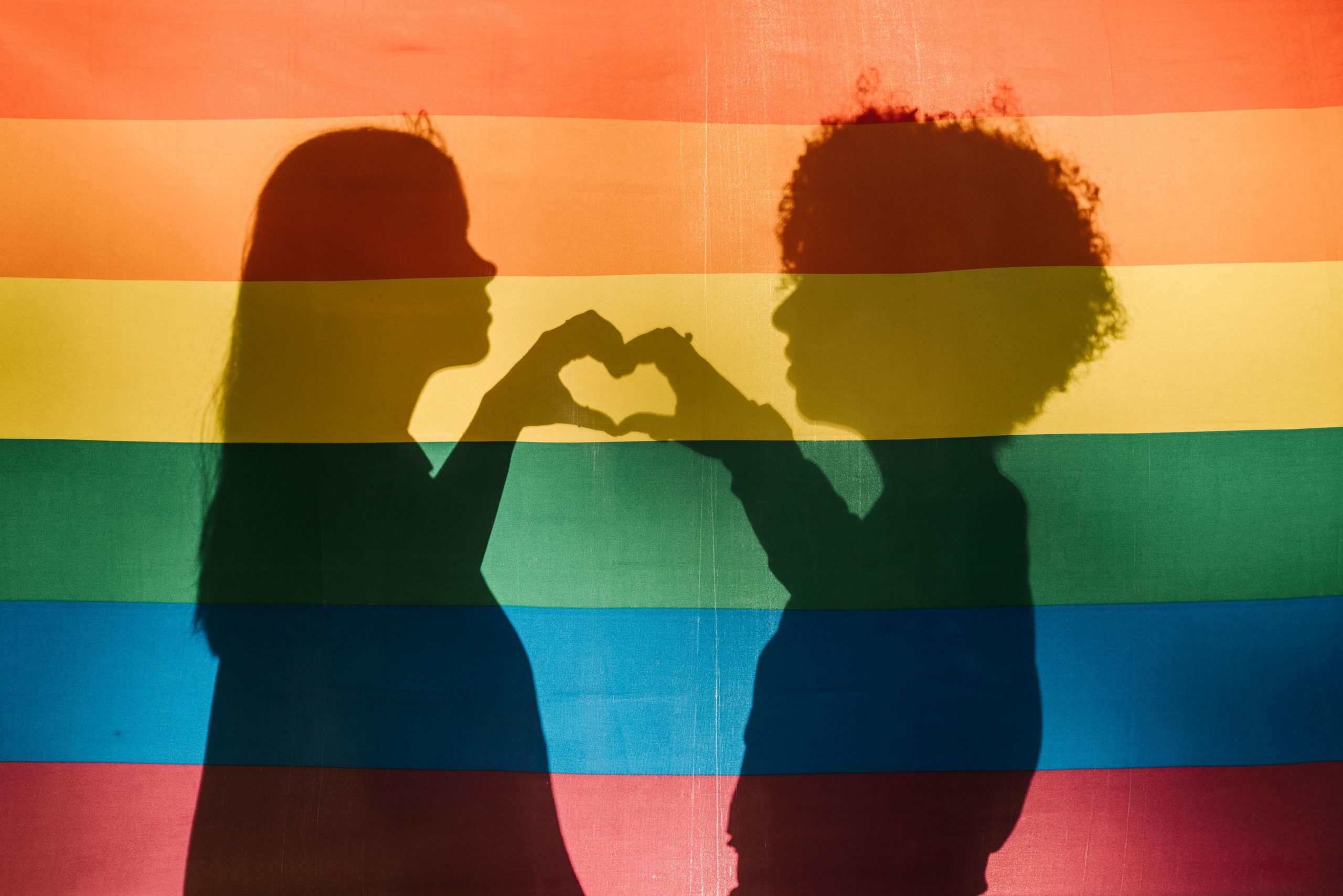 A pair of female lovers love hearts shadow cast on  rainbow flag