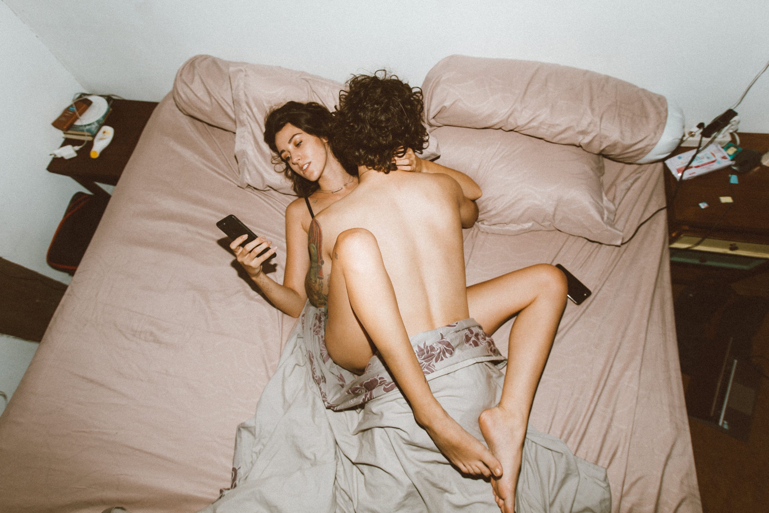 A woman and a man are making love in bed, but the woman is playing with her phone.