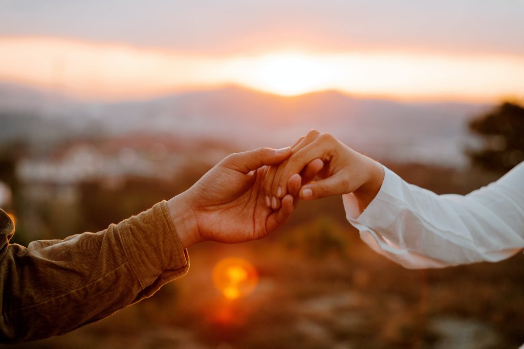 A boy gently holds a girl's hand in the sun.