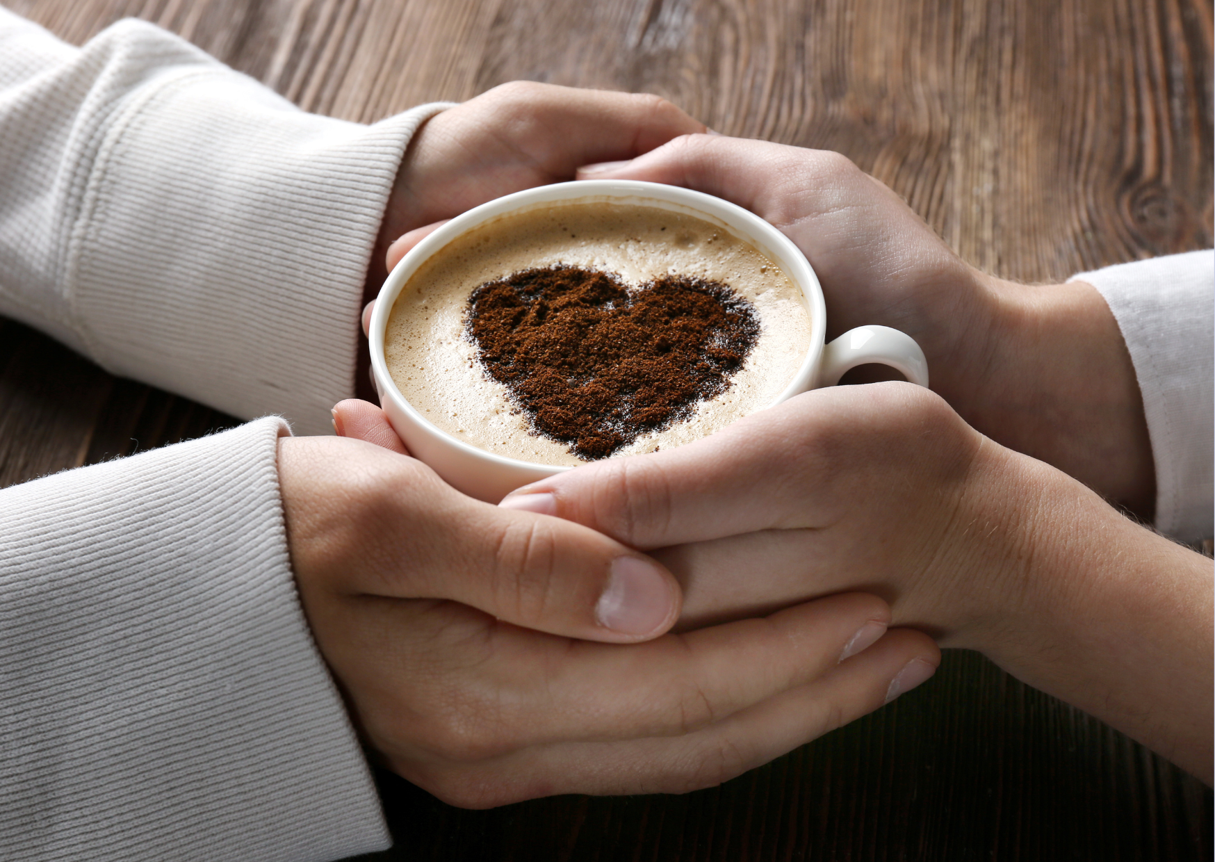 Two people holding a cup of coffee with a heart-shaped foam art, symbolizing a warm and cozy first date atmosphere.